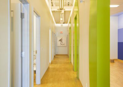 A bright, colorful hallway in a pediatric dental clinic, featuring green accents and playful wall art.