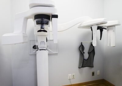 A close-up of a white dental Panorex machine for panoramic X-rays, with a protective vest hanging nearby