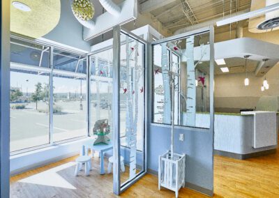 A well-lit waiting area with large windows, a children's play table, and a modern reception desk in the background.