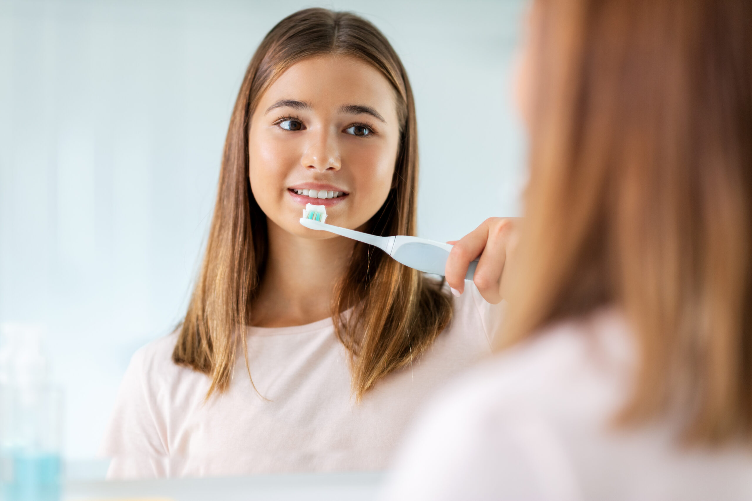 dental care, hygiene and people concept - happy smiling teenage girl with electric toothbrush brushing teeth at bathroom